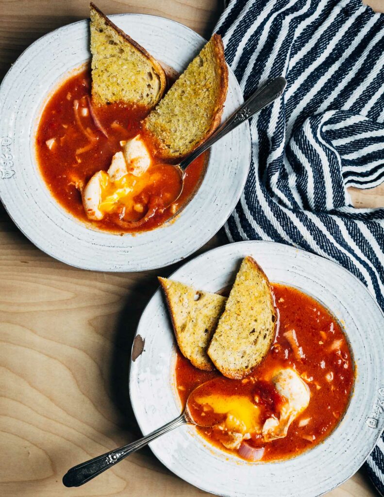 Tomatová polévka s vejcem a chlebem v bílém talíři. 