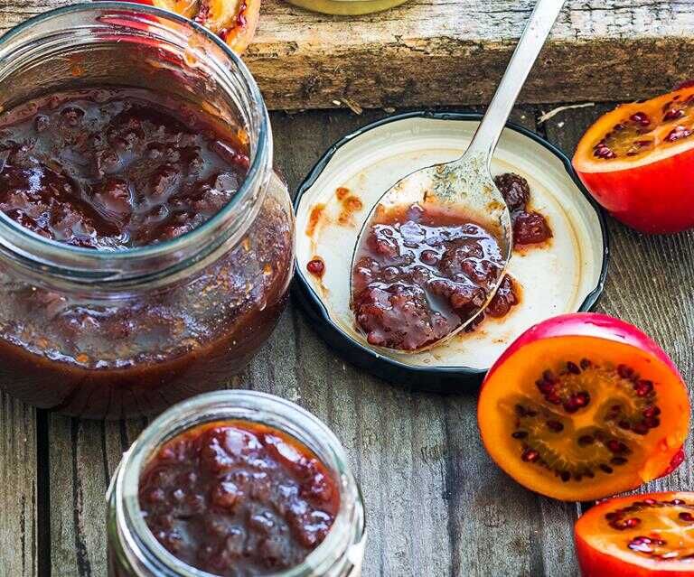 Džem z rajčenky ve sklenici a na lžíci s vedle položenou čerstvou rajčenkou.