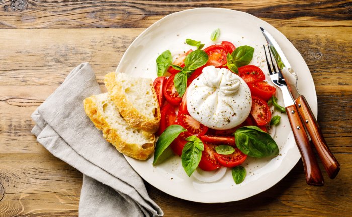 Burrata podávaná s rajčaty a lístky bazalky. 