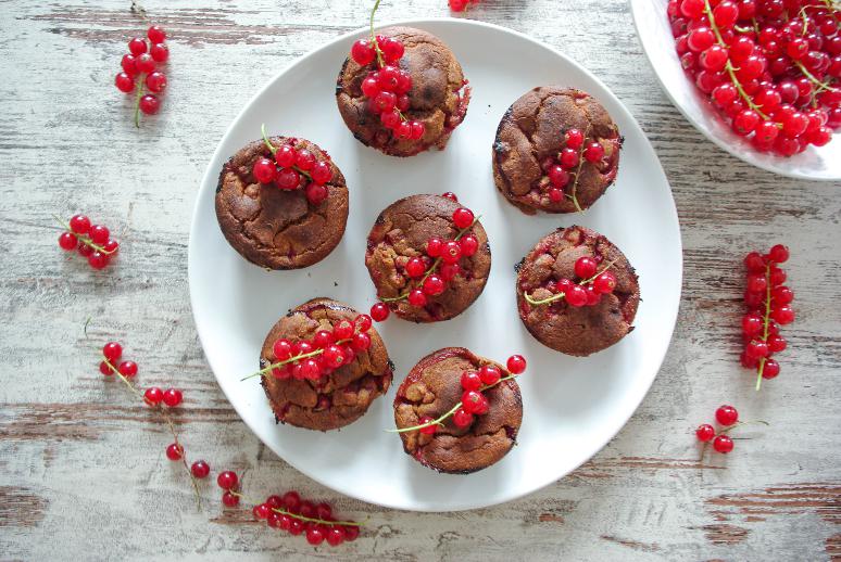 Muffiny ozdobené červeným rybízem servírované na talíři a vedle rozložený čerstvý rybíz.